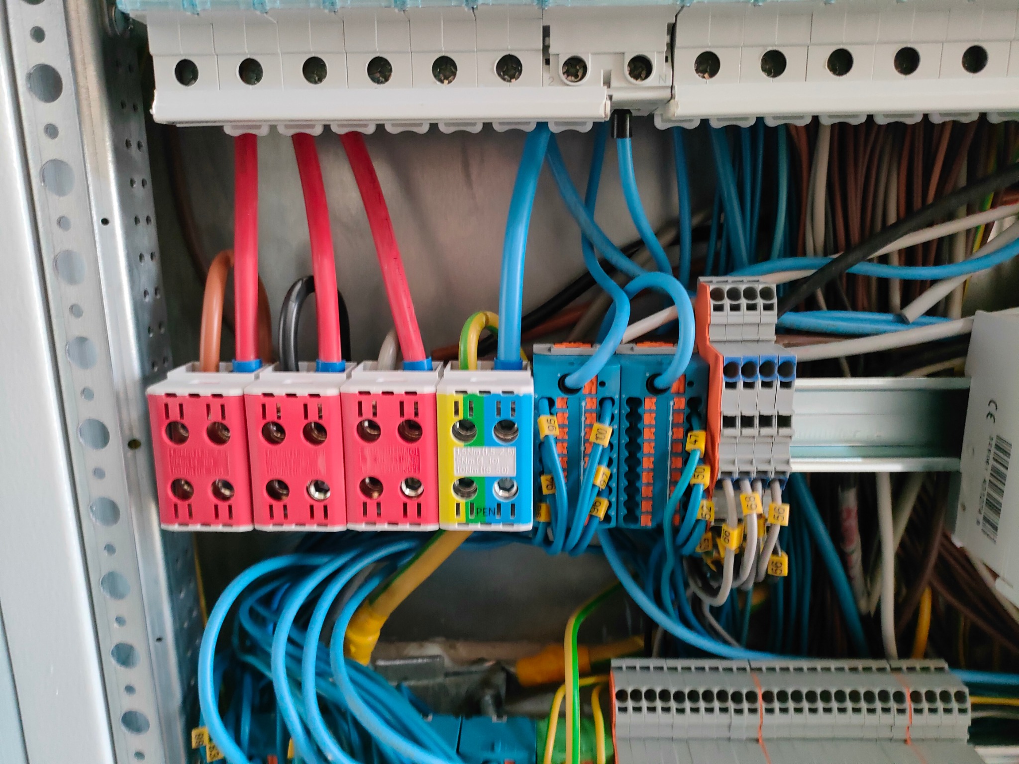 Rozdzielnica elektryczna z kolorowymi przewodami i złączkami, widoczne oznaczenia na kablach, z bliska.