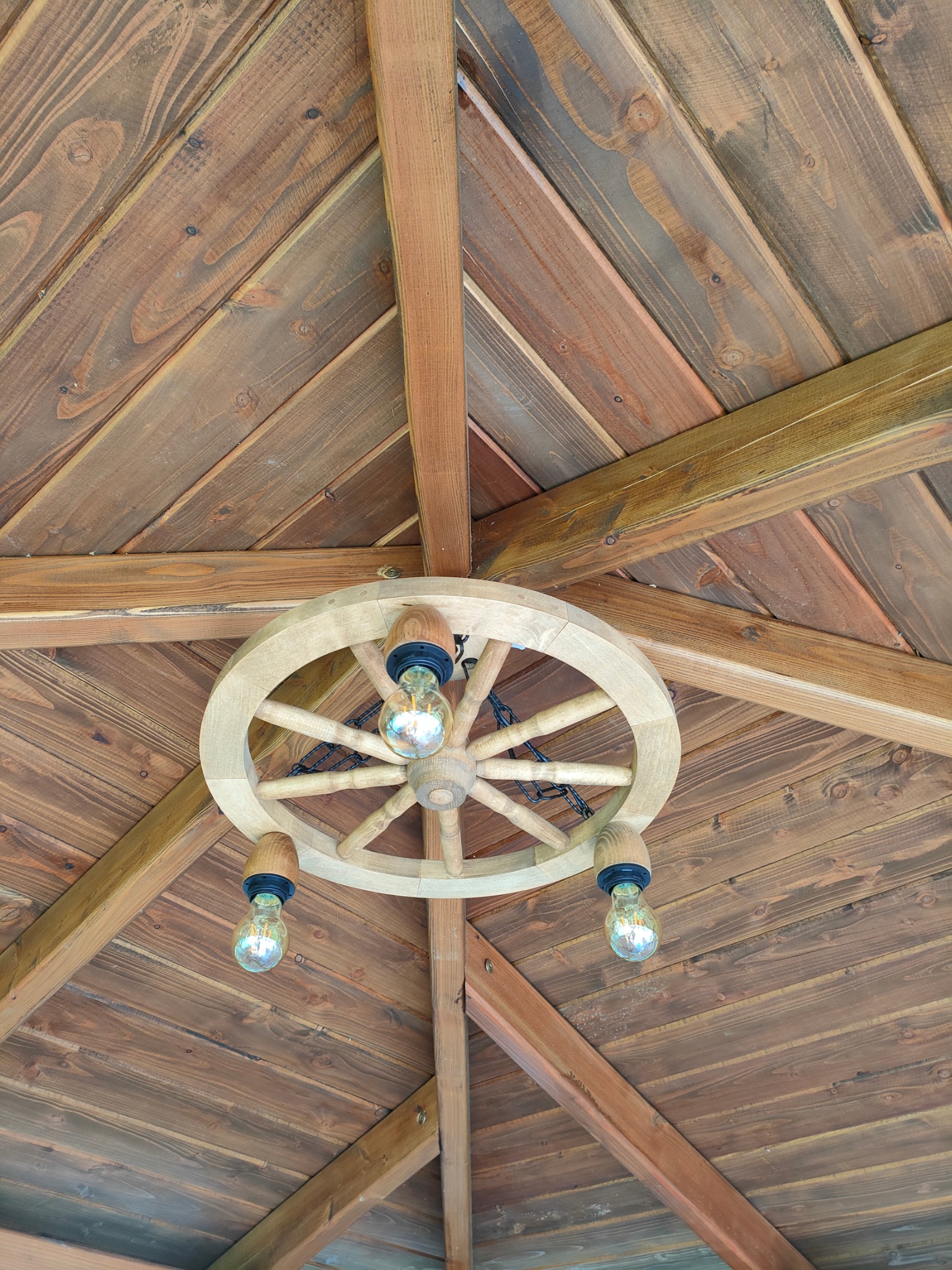 Drewniany sufit altany z dekoracyjną lampą w stylu koła od wozu z trzema żarówkami Edisona