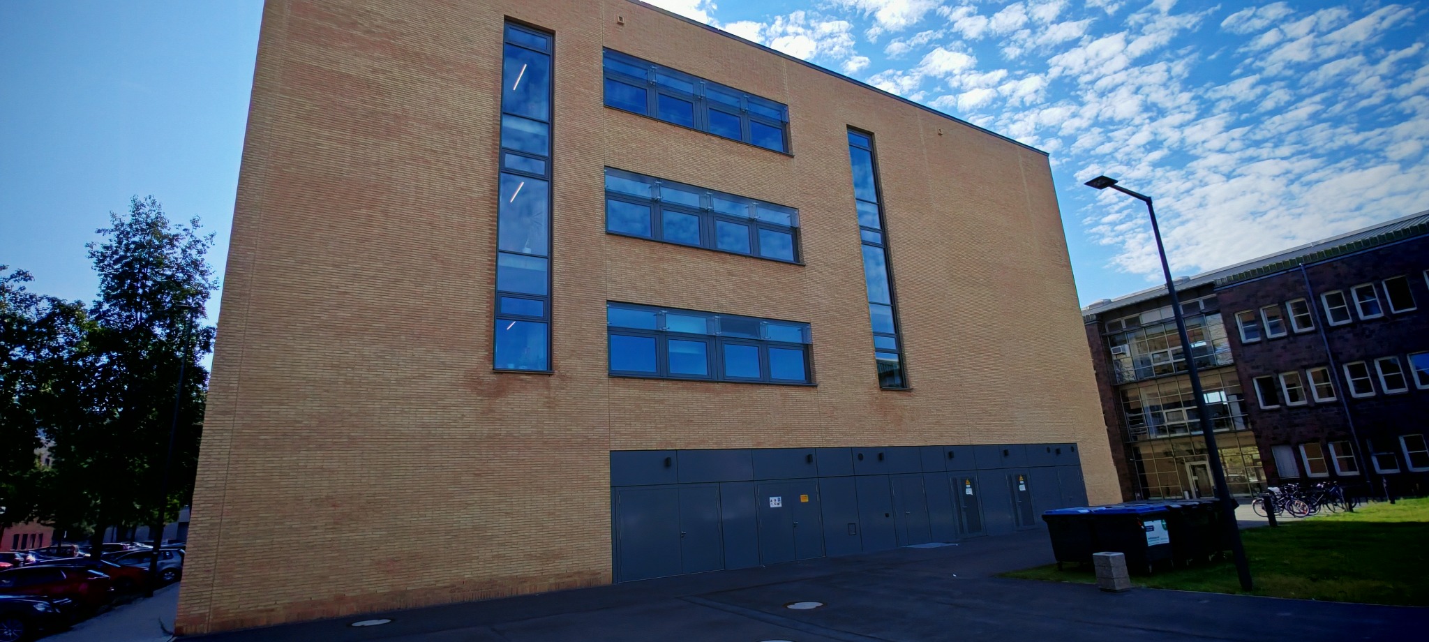 Fasada budynku z cegły klinkierowej z niebieskimi oknami i szarymi drzwiami na parterze, błękitne niebo z obłokami w tle.