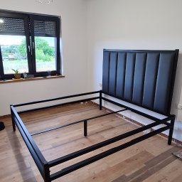 Mat&Art usługi spawalnicze Mateusz Zowisło - Rama metalowa łóżka z czarnym, tapicerowanym zagłówkiem w minimalistycznym wnętrzu z drewnianą podłogą i oknem z roletami.