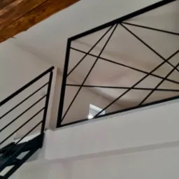 Schody z czarną, metalową konstrukcją i geometryczną balustradą wewnętrzną z widoczną drewnianą belką stropową