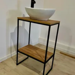 Umywalka nablatowa w białej misie na metalowym stelażu z drewnianymi p&oacute;łkami, czarna bateria, minimalistyczny design.