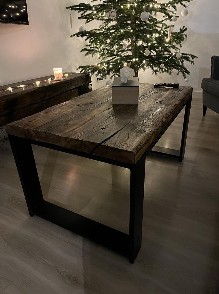 Stolik kawowy z blatem z postarzanego drewna i czarnymi, metalowymi nogami w minimalistycznym stylu, ustawiony w salonie z choinką w tle.