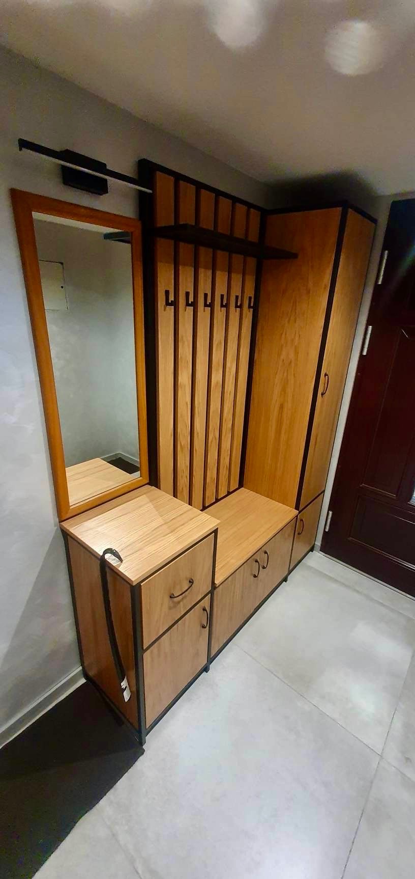 Funkcjonalna zabudowa przedpokoju z lustrem, w stylu loft, z drewnianymi elementami i czarnymi detalami, w tym wieszakami i obramowaniami.