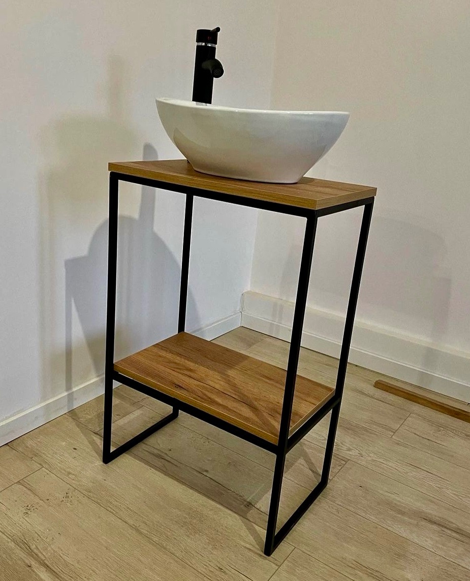 Umywalka nablatowa w białej misie na metalowym stelażu z drewnianymi półkami, czarna bateria, minimalistyczny design.