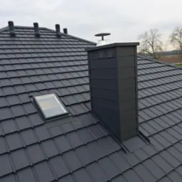 Grafitowy dach z blachodachówki z oknem dachowym i kominem wentylacyjnym, widoczne krople deszczu.