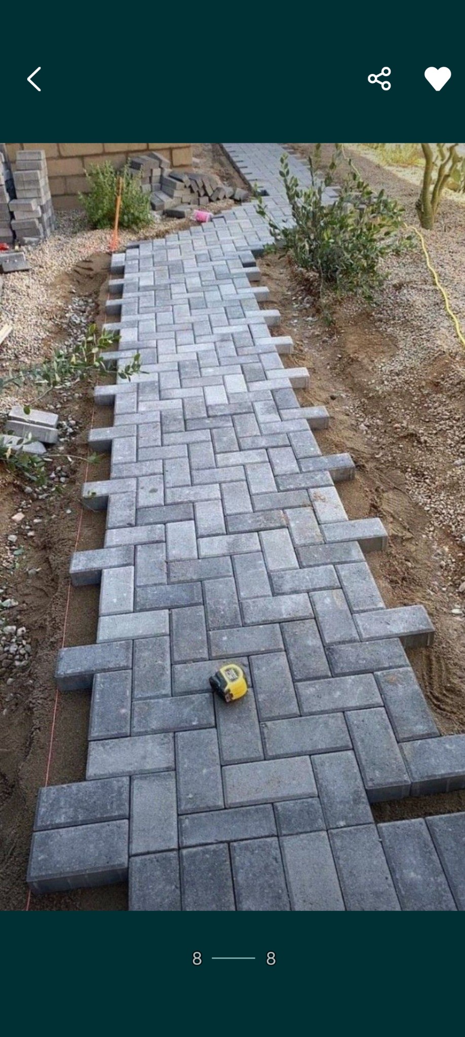 Ścieżka z szarej kostki brukowej w trakcie układania, widoczna żółta miarka i stos kostki w tle.