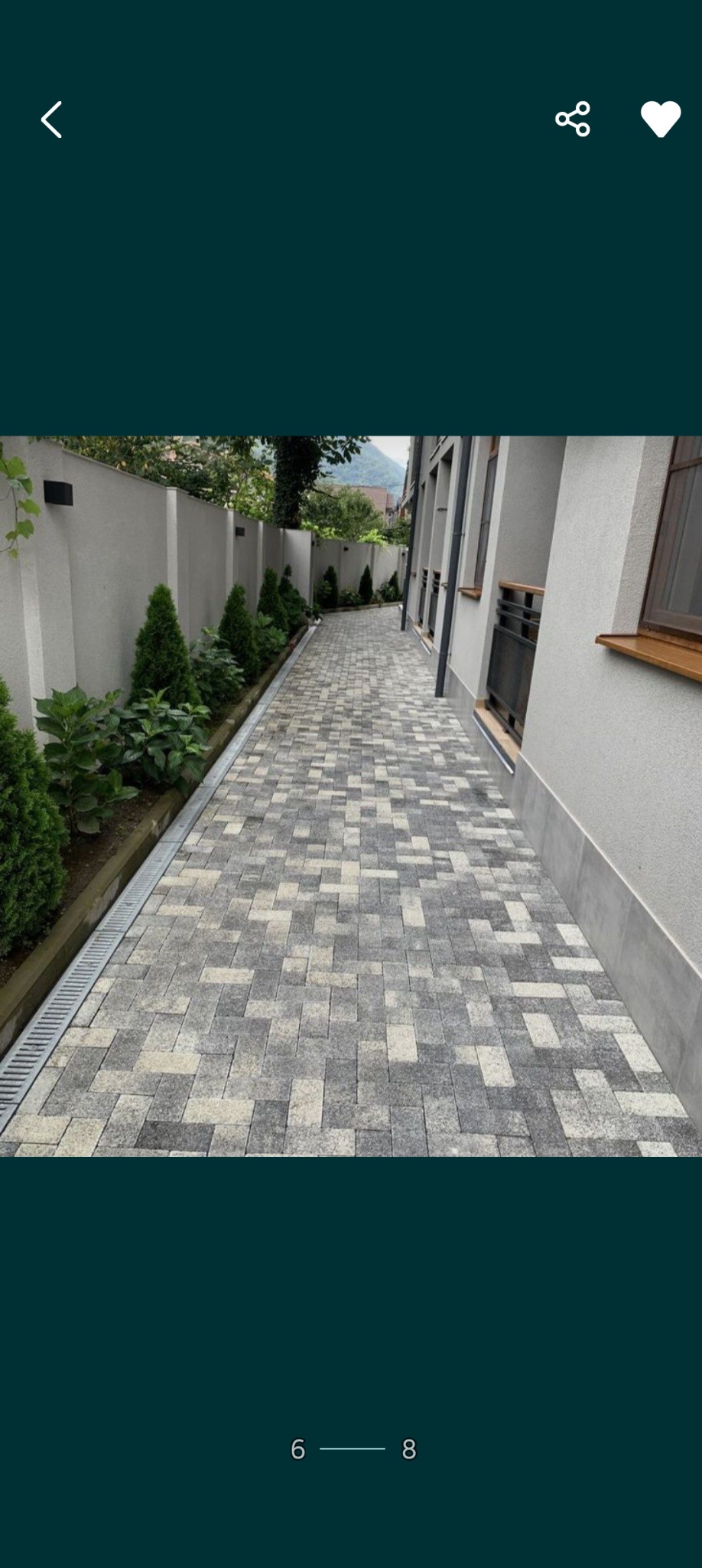 Ułożona szara kostka brukowa w jodełkę tworząca ścieżkę wzdłuż budynku z widocznym systemem odprowadzania wody i zadbaną roślinnością.