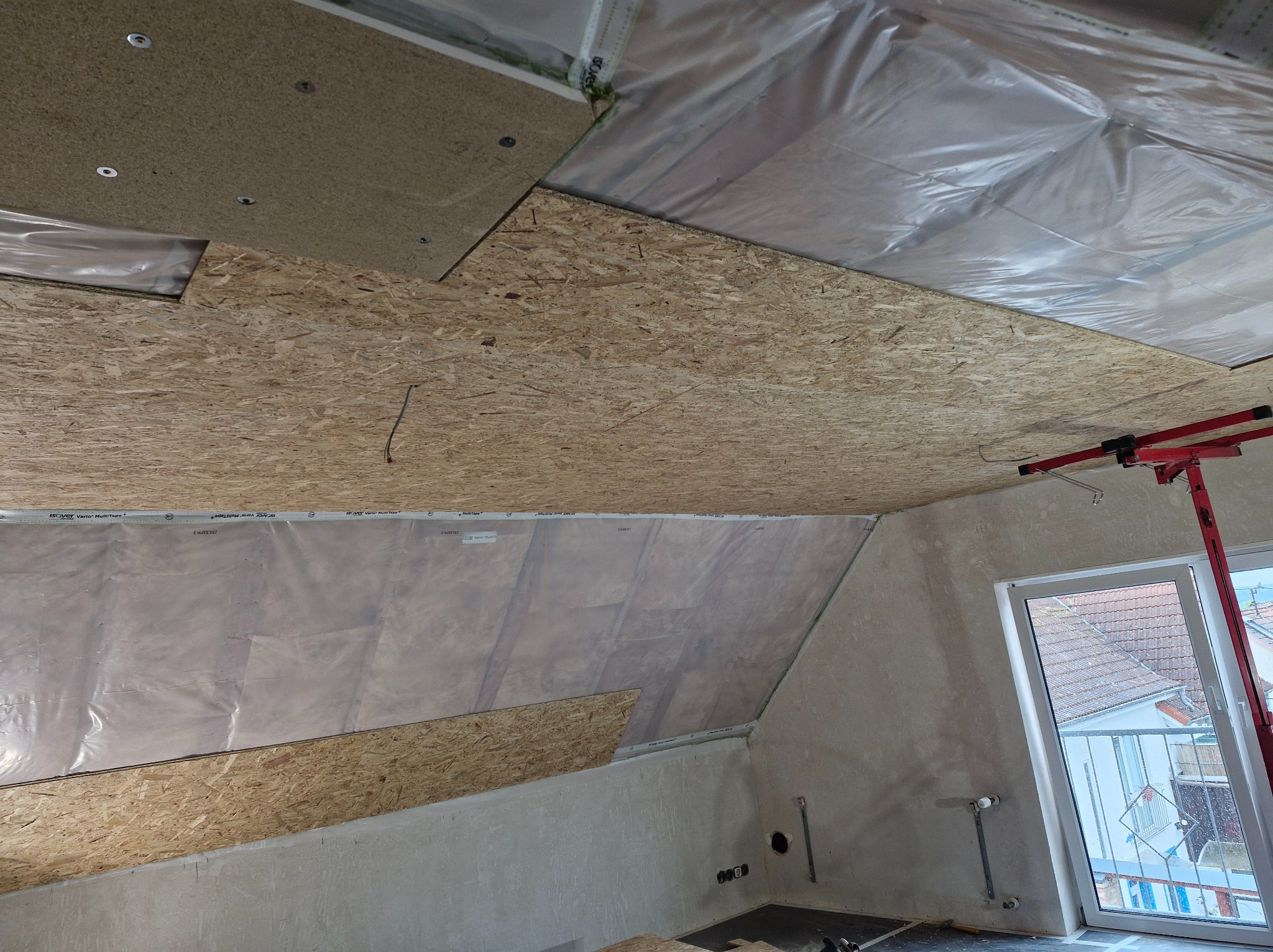 Montaż sufitu z płyt OSB na poddaszu, widoczna izolacja folią paroizolacyjną, konstrukcja metalowa oraz podnośnik do płyt, ściany w stanie surowym.