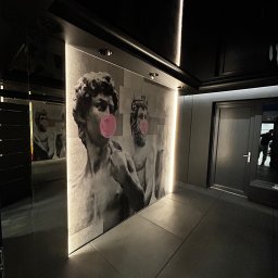 Marcin Suchański - Nowoczesne wnętrze z szarymi płytkami podłogowymi i ścianami ozdobionymi grafikami rzeźb z różowymi gumami balonowymi, oświetlone punktowo i listwami LED.