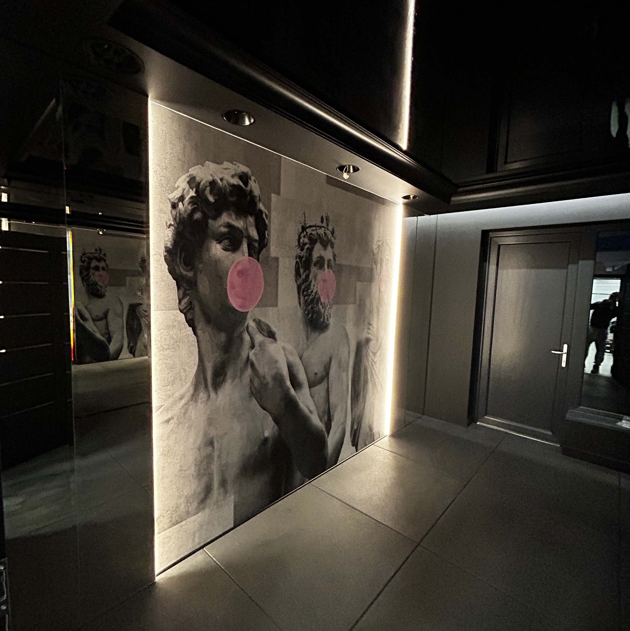 Nowoczesne wnętrze z szarymi płytkami podłogowymi i ścianami ozdobionymi grafikami rzeźb z różowymi gumami balonowymi, oświetlone punktowo i listwami LED.