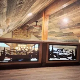 Drewniana balustrada z metalowymi panelami o wzorach górskich i leśnych, widoczna na tle drewnianego sufitu i kamiennej ściany. Unikalny detal w loftowym wnętrzu.