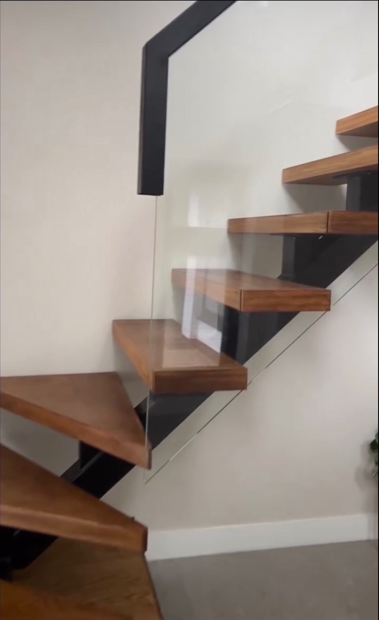 Nowoczesne schody drewniane z czarną metalową konstrukcją i szklaną balustradą, widok z dołu, minimalistyczny design.