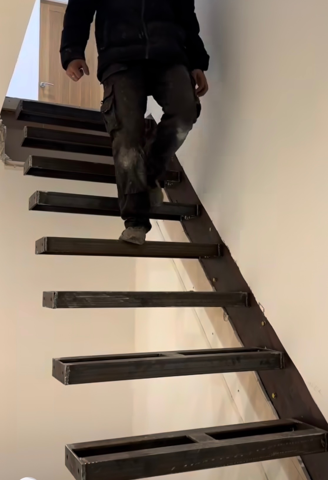 Montaż ażurowych schodów z metalowych profili; widoczny pracownik w ubraniu roboczym w trakcie wchodzenia po nieukończonej konstrukcji.