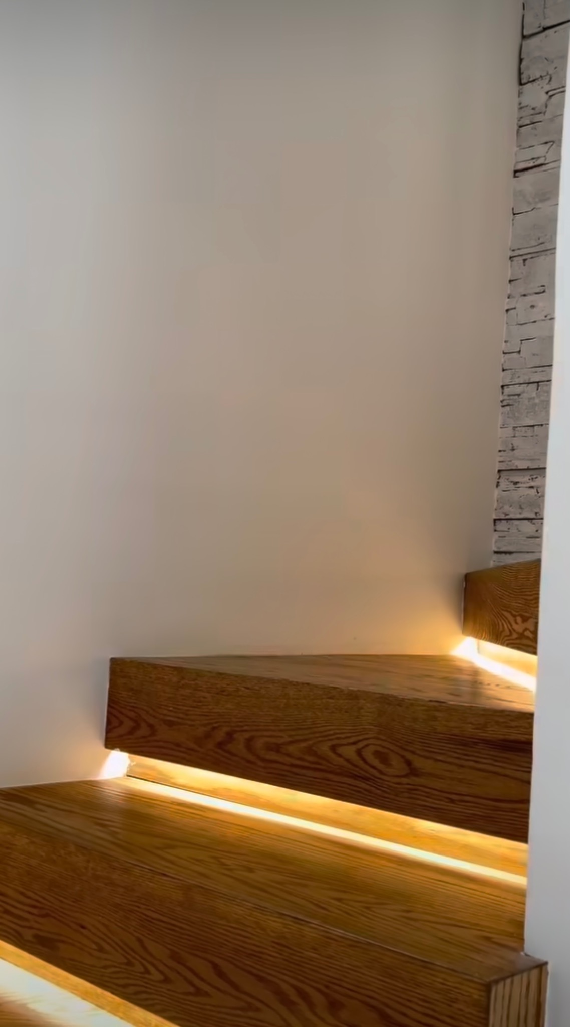 Nowoczesne schody z drewna z podświetleniem LED, widok z dołu, jasne drewno z wyraźnym usłojeniem, biała ściana w tle.