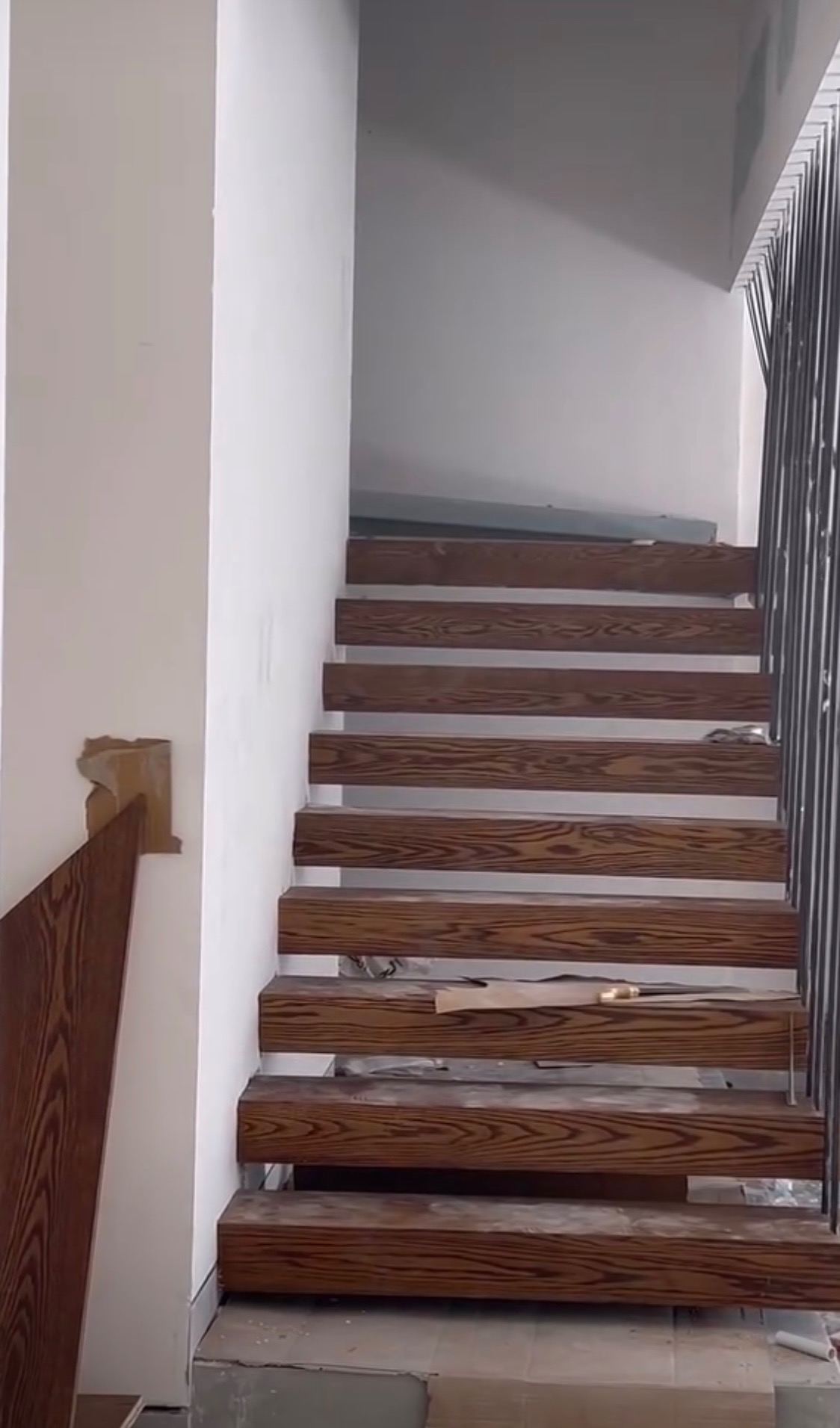 Montaż drewnianych schodów wspornikowych z ciemnego drewna, widoczne elementy konstrukcyjne i niedokończone wykończenie ścian.