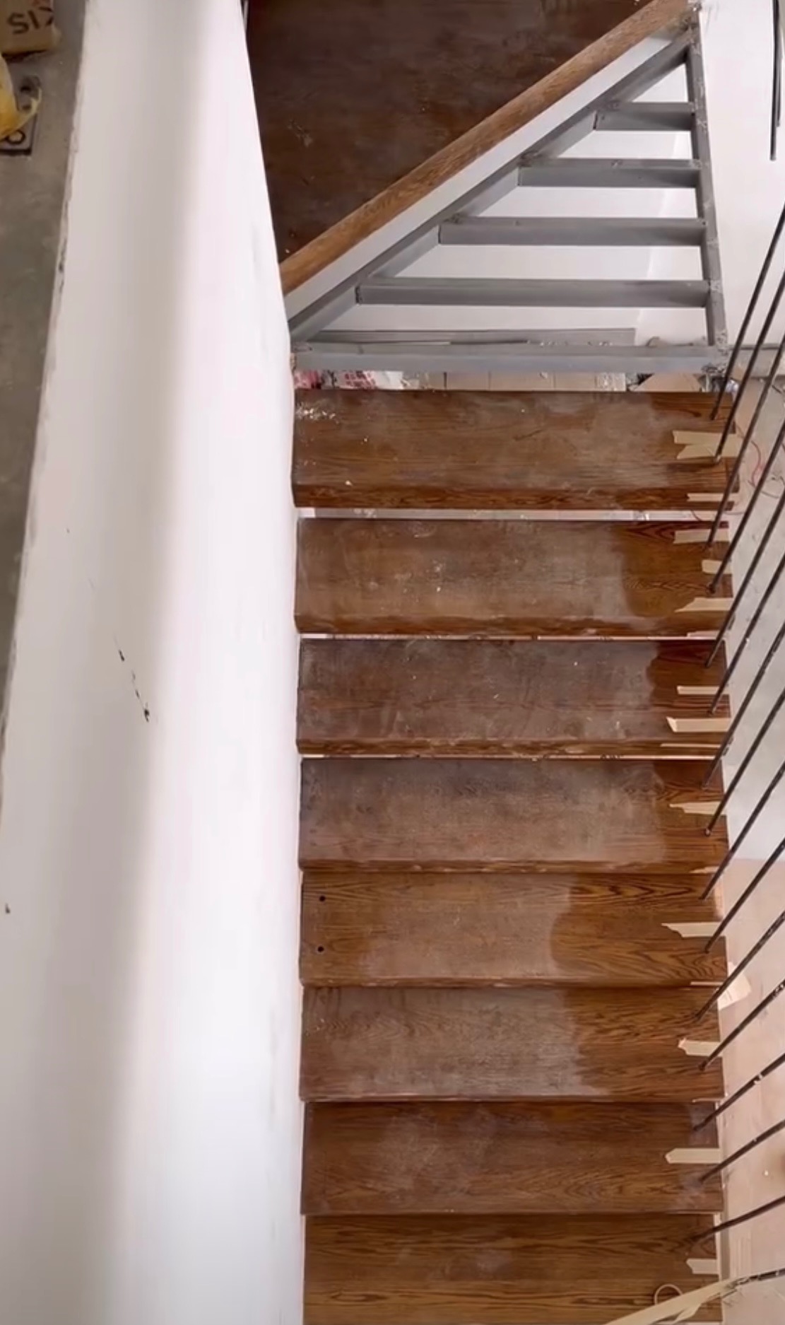 Wewnętrzne schody z drewnianymi stopniami i metalową konstrukcją nośną, widok z góry na etapie montażu poręczy.