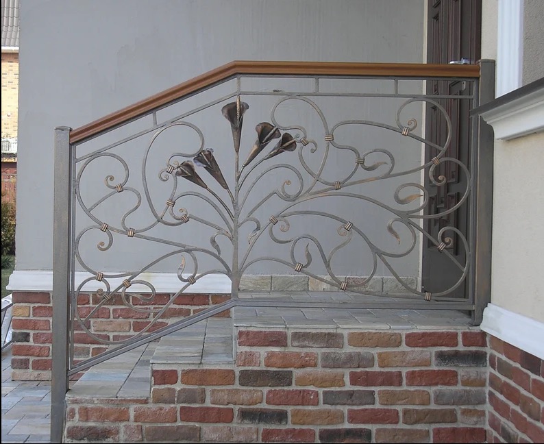 Kute balustrady schodowe z motywem roślinnym kalii, drewniany pochwyt, ceglana podstawa schodów, szara ściana w tle. Detal wykonania.