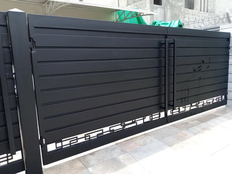 Nowoczesna, czarna brama przesuwna z poziomymi panelami i geometrycznym wzorem u dołu, na tle surowego budynku.