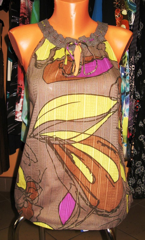 Letnia bluzka bez rękawów z abstrakcyjnym wzorem kwiatowym w odcieniach brązu, żółci i fioletu, prezentowana na manekinie z wykończeniem z szarej koronki przy dekolcie.