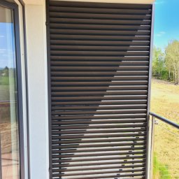 DiM Studio - Balkon z nowoczesną, poziomą, metalową przesłoną w kolorze antracytowym, zapewniającą prywatność, z widokiem na zielone wzgórza i błękitne niebo.