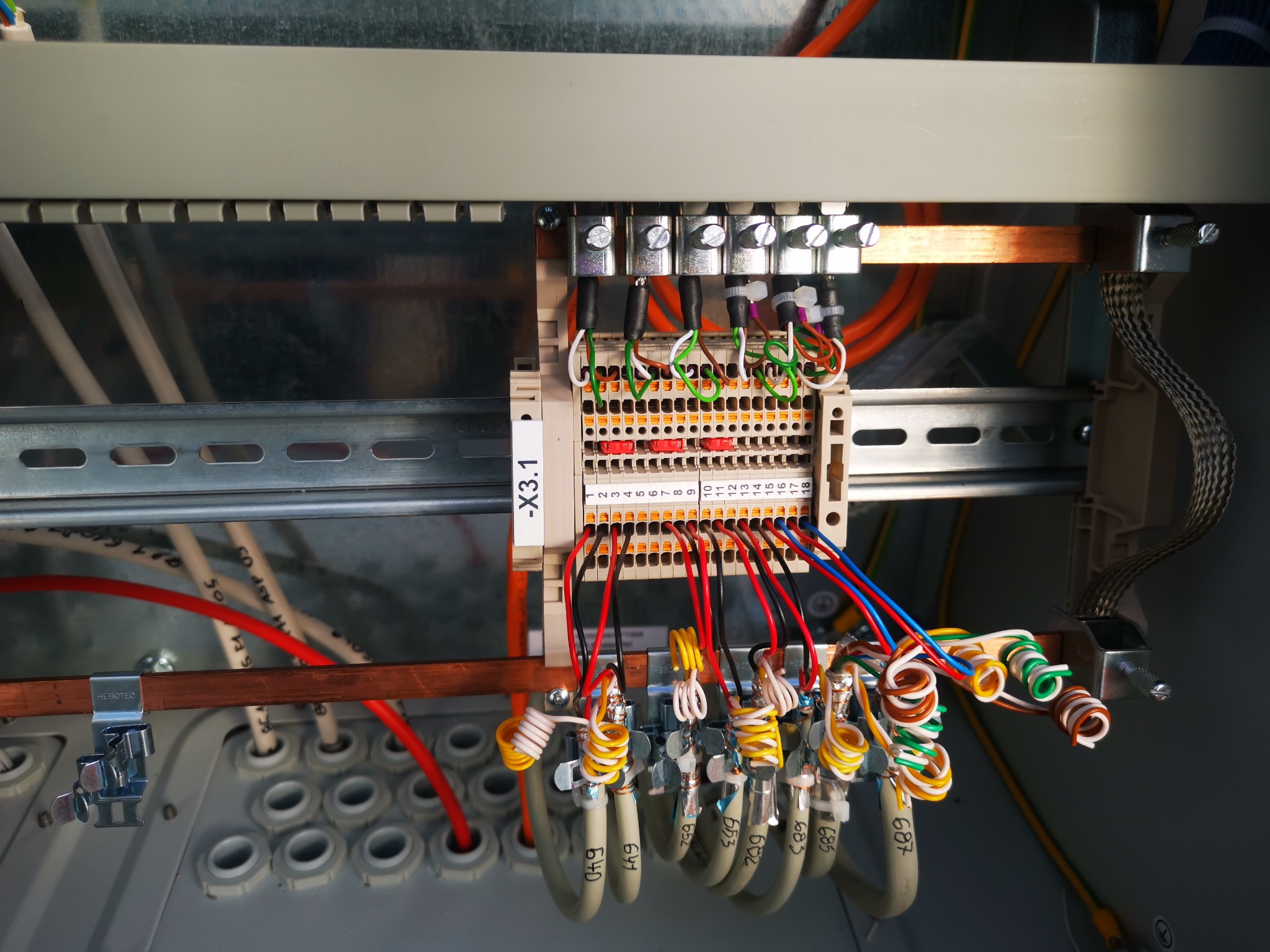 Panel sterowania z precyzyjnie ułożonymi przewodami oznaczonymi numerami, podłączonymi do listwy zaciskowej. Widoczne szyny montażowe i elementy mocujące.