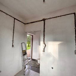 INSTALATORSTWO ELEKTRYCZNE Artur Marański - Wnętrze w trakcie remontu z nową instalacją elektryczną prowadzoną po ścianach, zabezpieczoną szarym cementem, widoczna drabina aluminiowa.