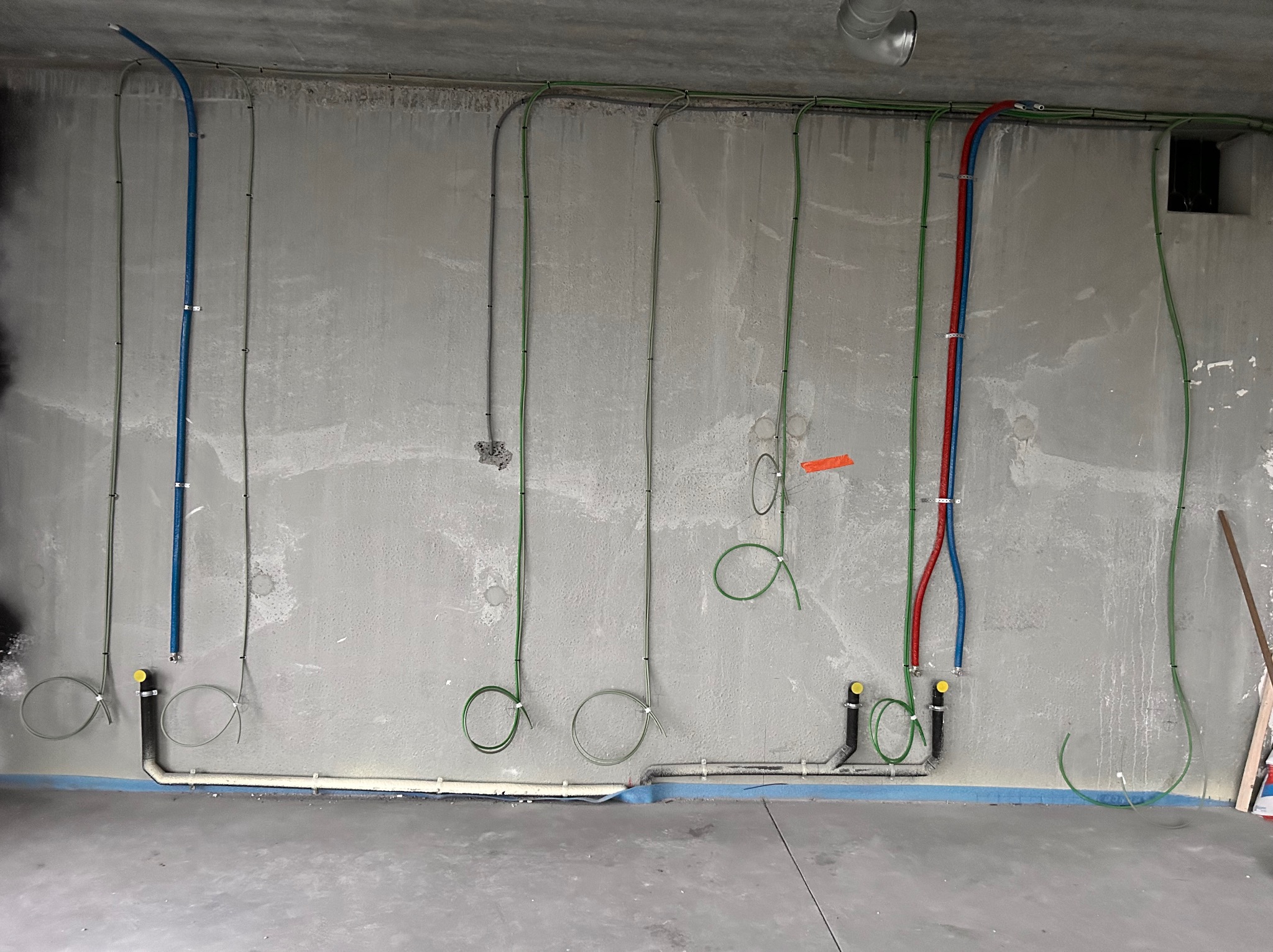 Surowa ściana z widocznymi instalacjami elektrycznymi i wodno-kanalizacyjnymi w trakcie montażu w Jasionowie. Widoczne kable i rury prowadzone po ścianie, niektóre zakończone zaślepkami.