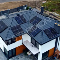 Widok z g&oacute;ry na nowoczesny dom z szarym dachem pokrytym panelami słonecznymi, zlokalizowany we Włocławku, z widocznym fragmentem ogrodu i ogrodzenia.