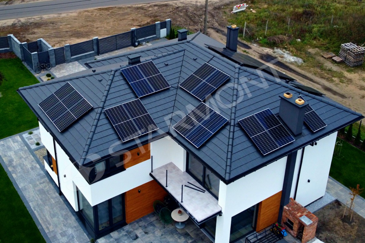 Widok z góry na nowoczesny dom z szarym dachem pokrytym panelami słonecznymi, zlokalizowany we Włocławku, z widocznym fragmentem ogrodu i ogrodzenia.