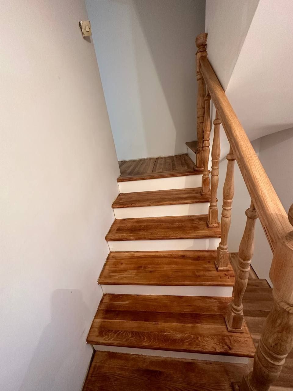 Odnowione drewniane schody z białymi podstopnicami i jasną, lakierowaną balustradą, widok z dołu, ściana pomalowana na biało.