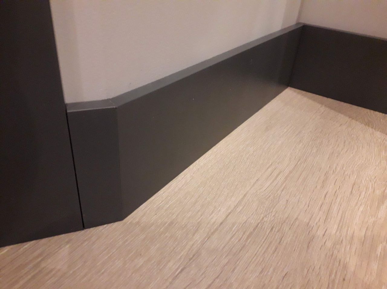 Szczegółowo wykonane połączenie szarej listwy przypodłogowej z jasną podłogą, widoczne precyzyjne cięcia pod kątem.