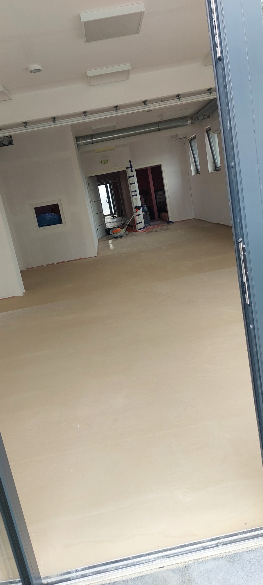 Wnętrze pomieszczenia z wylewką samopoziomującą przed dalszymi pracami wykończeniowymi podłogi, widoczna szpachla na ścianach, okna i drzwi.