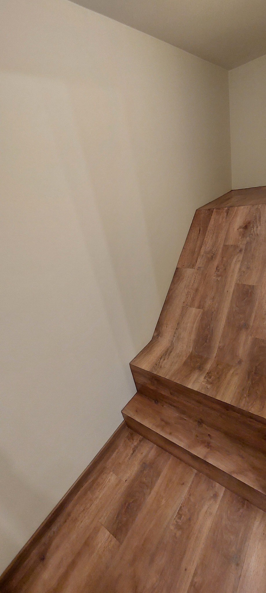 Wykończone schody z paneli podłogowych o wzorze drewna, przylegające do jasnej ściany, widok z góry pod kątem.