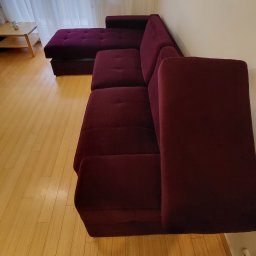 Czysty Mebel - Burgundowa, narożna kanapa z aksamitną tapicerką na parkiecie w mieszkaniu w Warszawie, widok z boku.