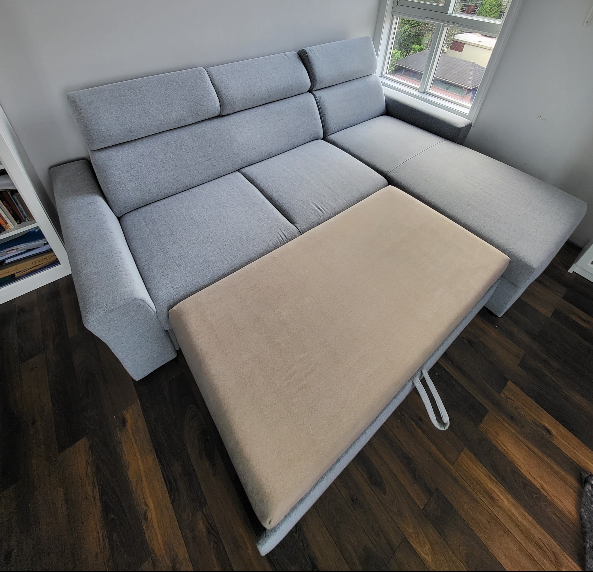 Rozłożona szara kanapa narożna z wysuniętym beżowym elementem do spania, widok z góry na parkiet.