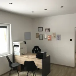 Jasne biuro z drewnianym biurkiem, czarnymi krzesłami i ścianą z certyfikatami, oświetlone punktowymi lampami sufitowymi.