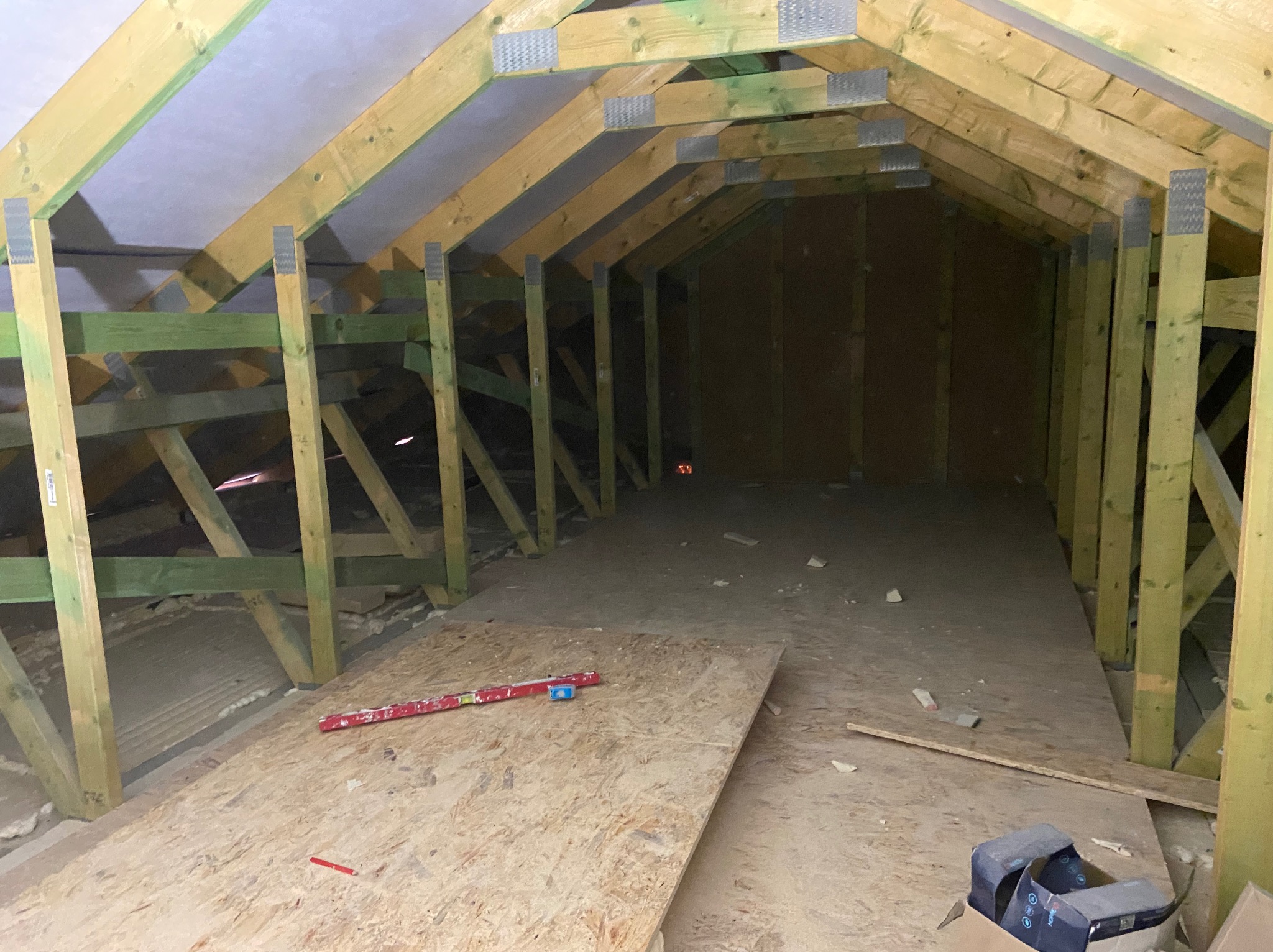 Konstrukcja drewniana poddasza z widocznymi elementami ocieplenia, poziomica leżąca na płycie OSB i karton w rogu kadru.