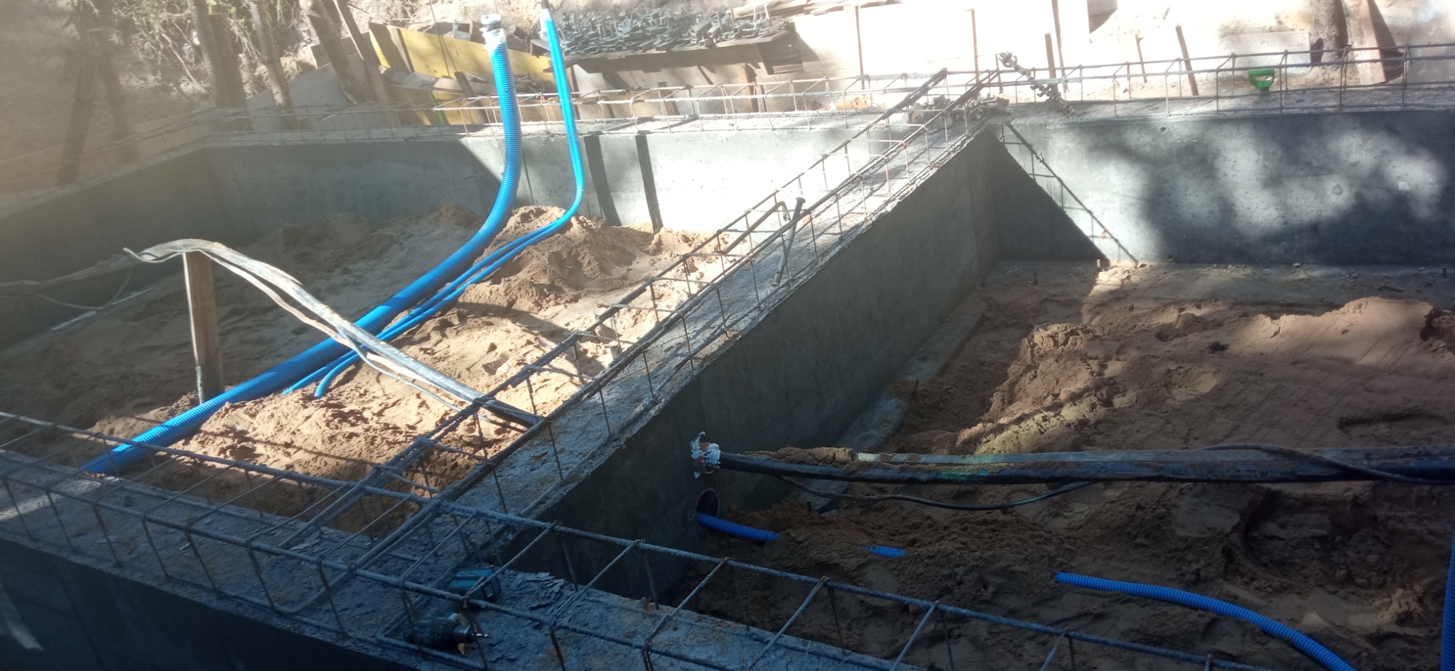 Fundamenty budynku w trakcie budowy z widocznymi niebieskimi rurami karbowanymi do rozprowadzenia instalacji elektrycznej w ziemi.