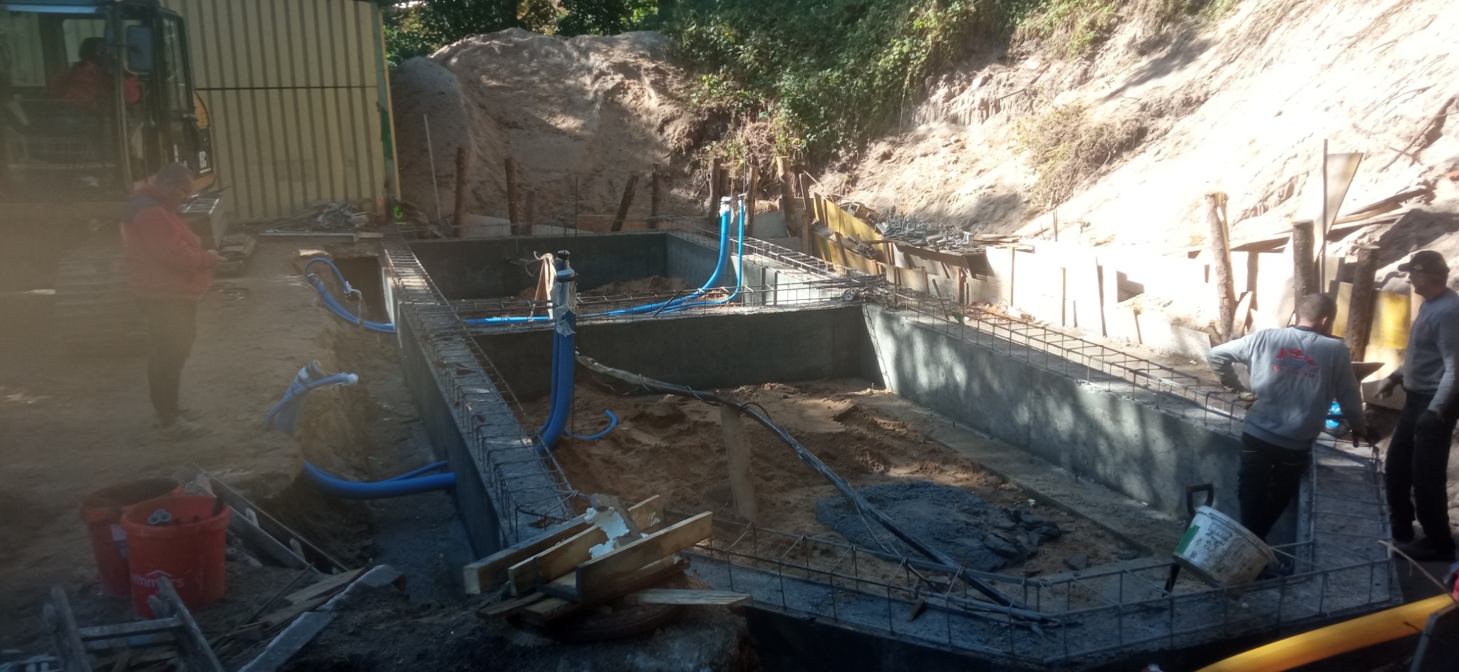 Budowa fundamentów pod budynek z widocznymi rurami instalacji elektrycznej w ziemi i pracownikami w tle.