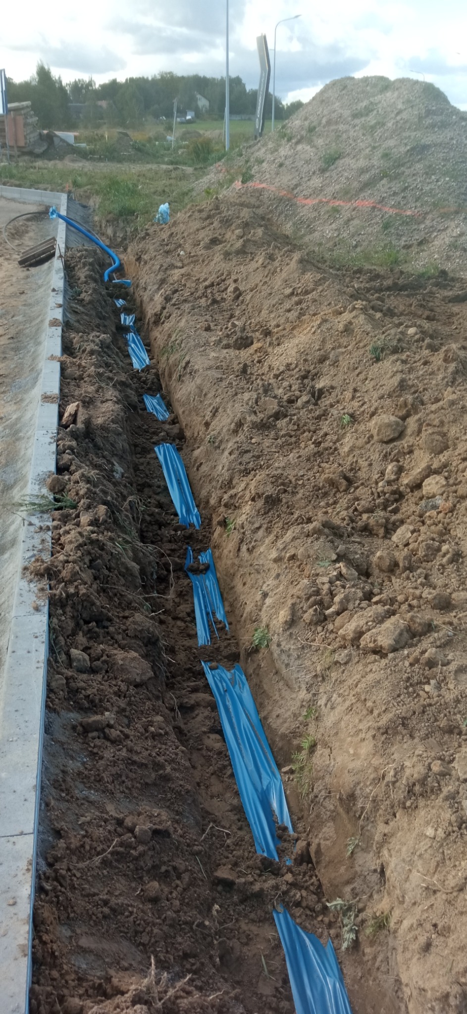 Wykop w ziemi z ułożonymi niebieskimi rurami w osłonie, widoczne elementy instalacji podziemnej w trakcie budowy.
