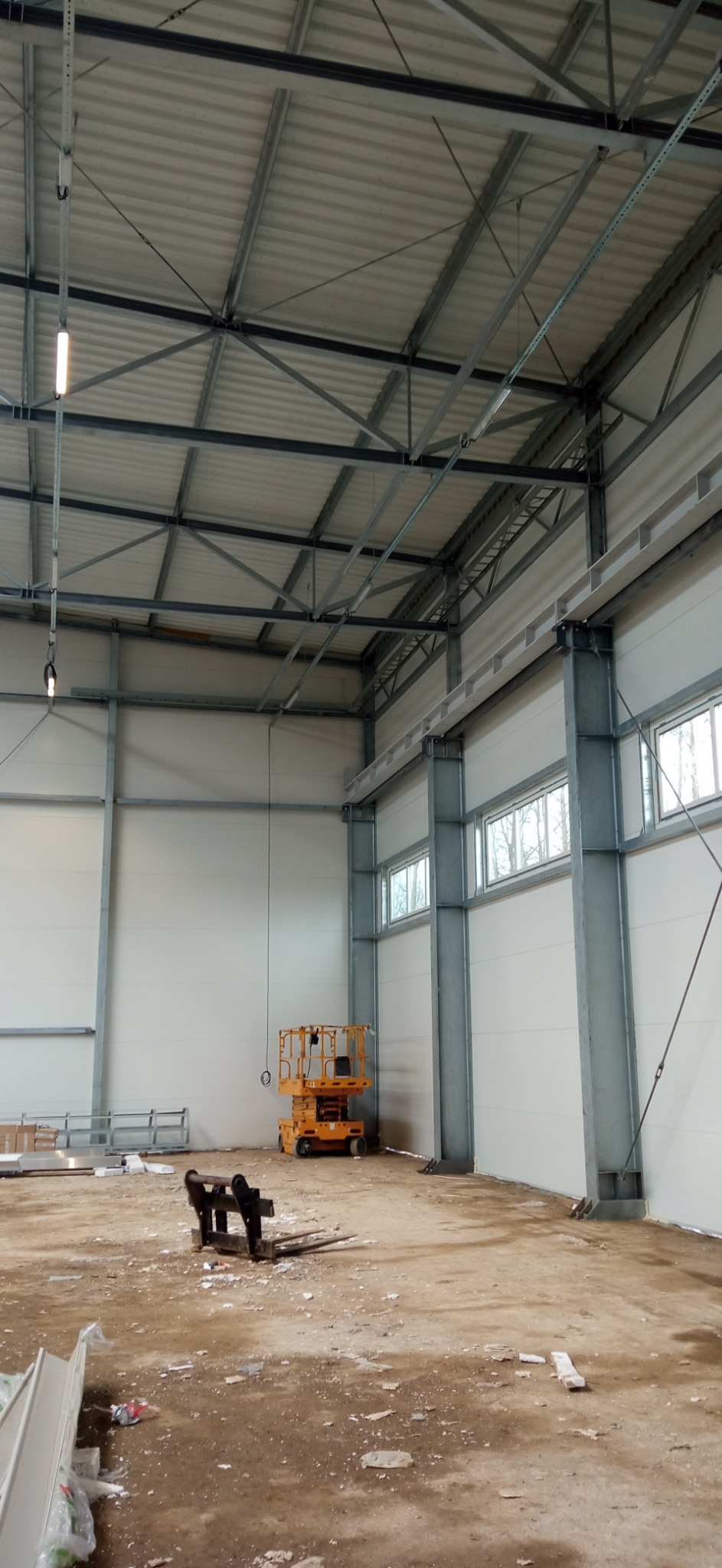 Wnętrze hali produkcyjnej w trakcie prac, widoczna podnośnik koszowy i elementy konstrukcji pod sufitem, prawdopodobnie w trakcie montażu instalacji.