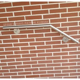 Spaw Serwis Patryk Kubiak - Przymocowana do ceglanej ściany, pochylona, metalowa poręcz schodowa z widocznymi mocowaniami.