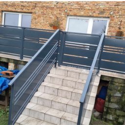 Spaw Serwis Patryk Kubiak - Metalowa balustrada schodowa w kolorze grafitowym, z poziomymi szczeblami, prowadząca do wejścia domu z cegły.
