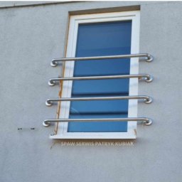 Spaw Serwis Patryk Kubiak - Zewnętrzne, metalowe, spawane zabezpieczenie okna z czterech poziomych prętów mocowanych do ściany budynku. Widoczne spawy i szlifowania. Na dole okna napis 'SPAW SERWIS PATRYK KUBIAK'.