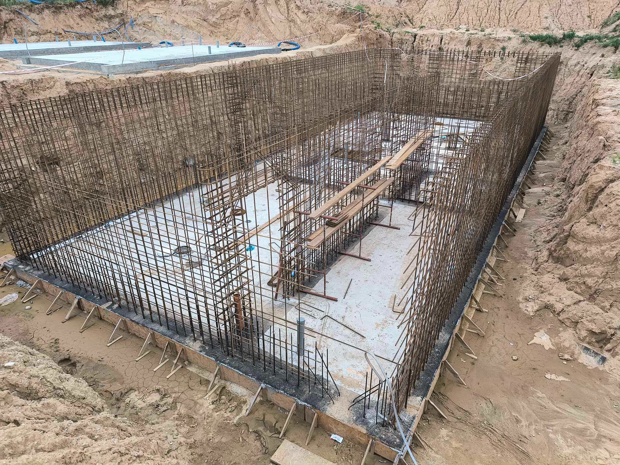 Zbrojenie pionowe i poziome fundamentu w wykopie, z widoczną płytą betonową i deskowaniem, przygotowane do zalania betonem.