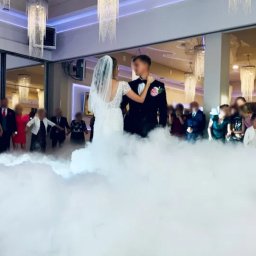 Dmytro Sokolov - Para młoda tańczy pierwszy taniec w chmurach dymu na tle gości i eleganckich żyrandoli. Dekoracja sali weselnej.