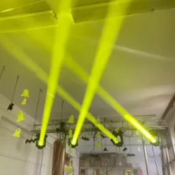 Żółte reflektory oświetlają dekoracje Halloween, w tym duchy i nietoperze, zawieszone na metalowej konstrukcji. Scena przygotowana na imprezę.