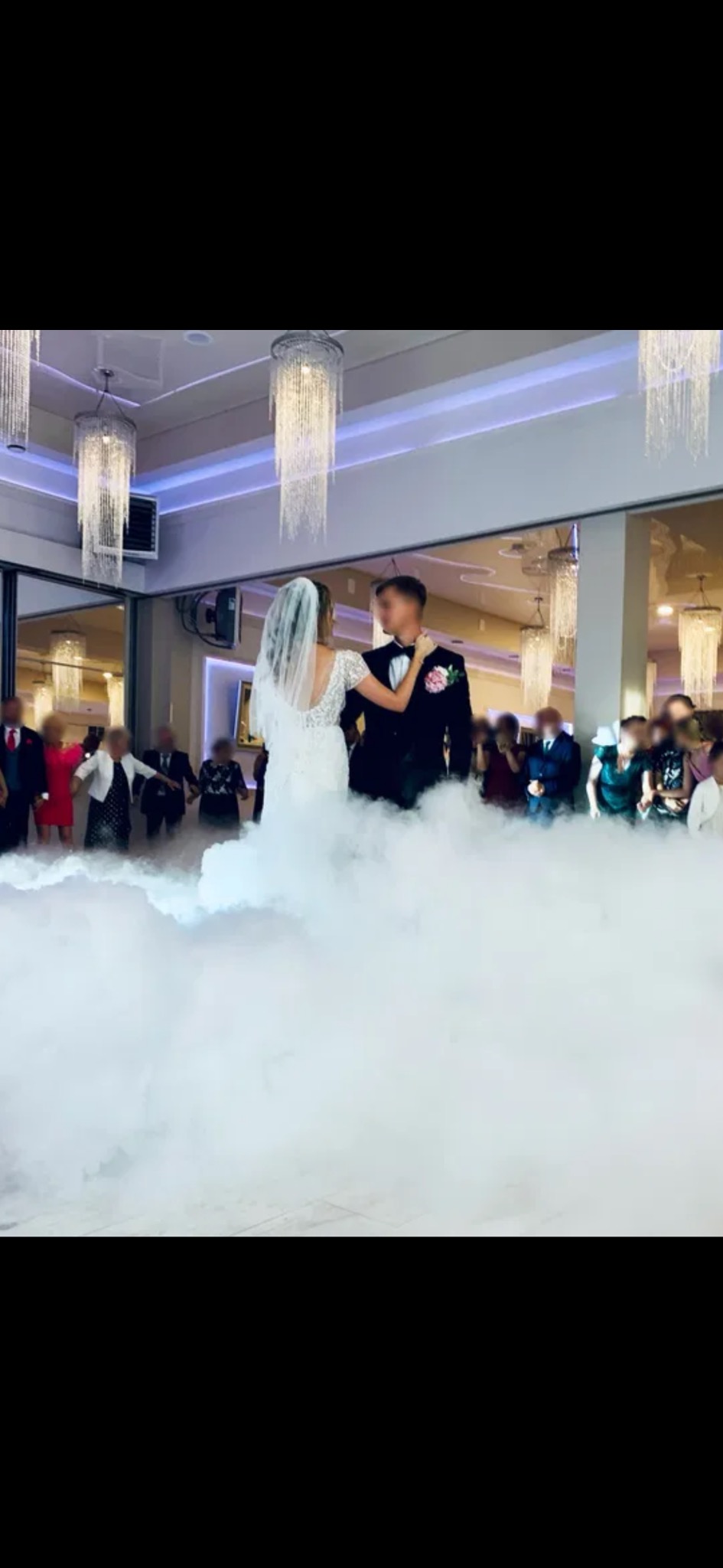 Para młoda tańczy pierwszy taniec w chmurach dymu na tle gości i eleganckich żyrandoli. Dekoracja sali weselnej.