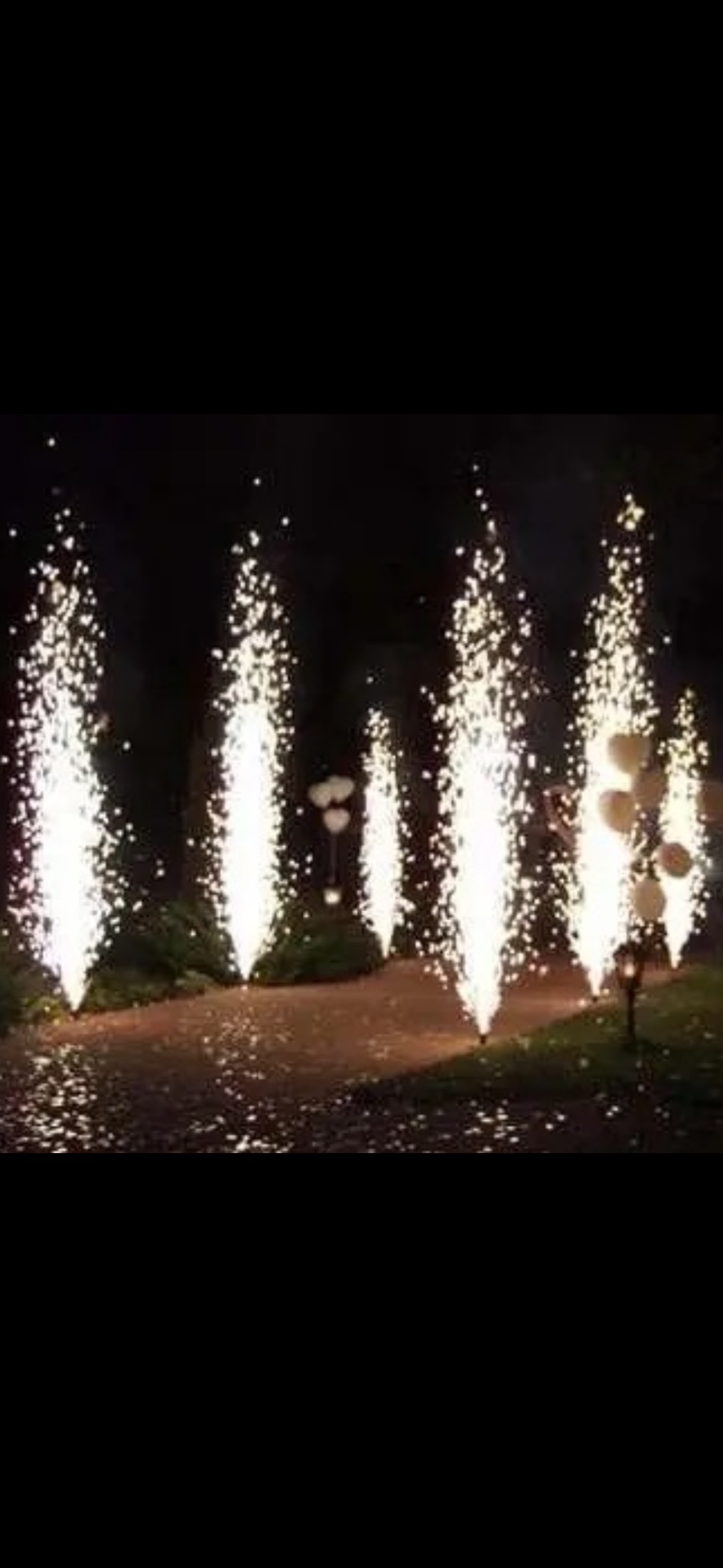 Fontanny iskier na ścieżce, wieczorowa dekoracja plenerowa z białymi balonami w tle, tworzące magiczną atmosferę.